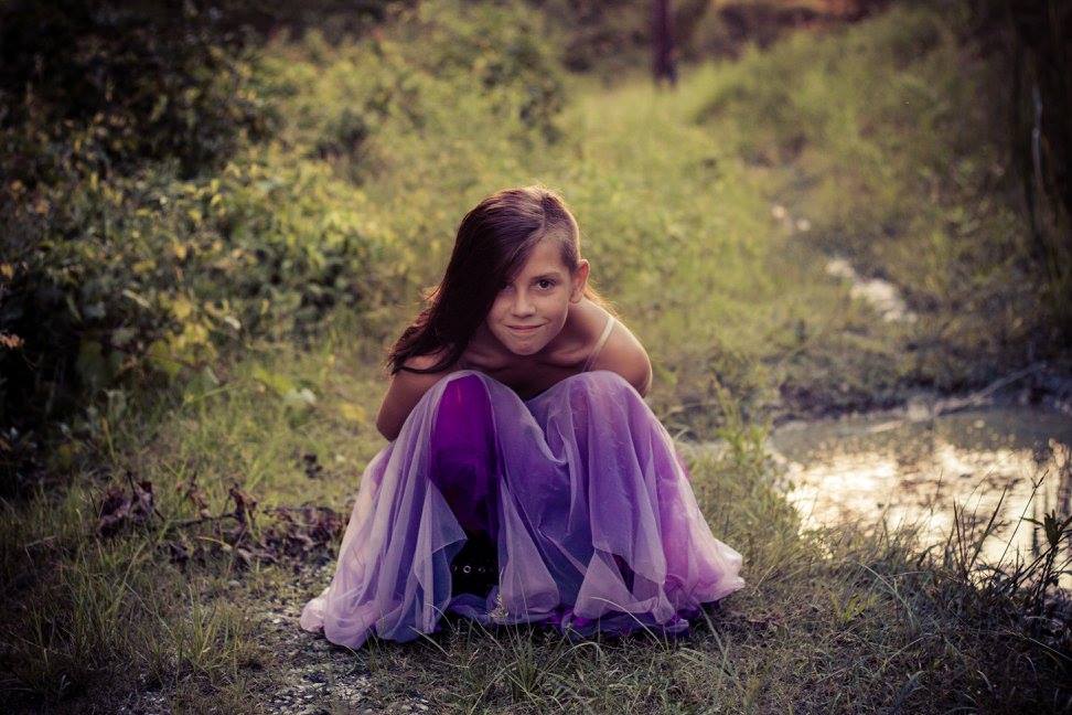 Evening scene in Denham Springs. Girl squatting next to pond smiling.